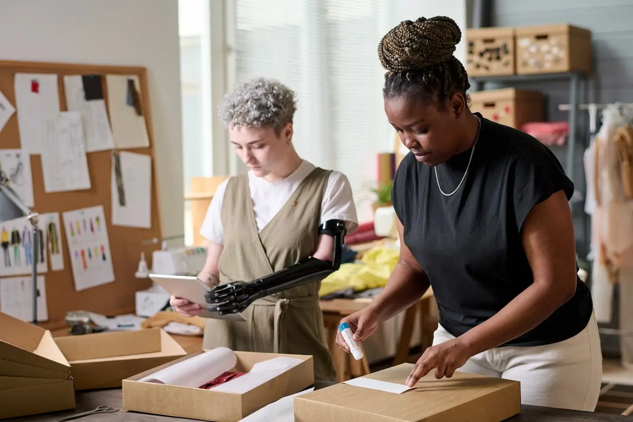 Two women, one with a prosthetic arm, are packaging boxes in a design studio; this scene brings to mind the question, "What does AOV mean?"