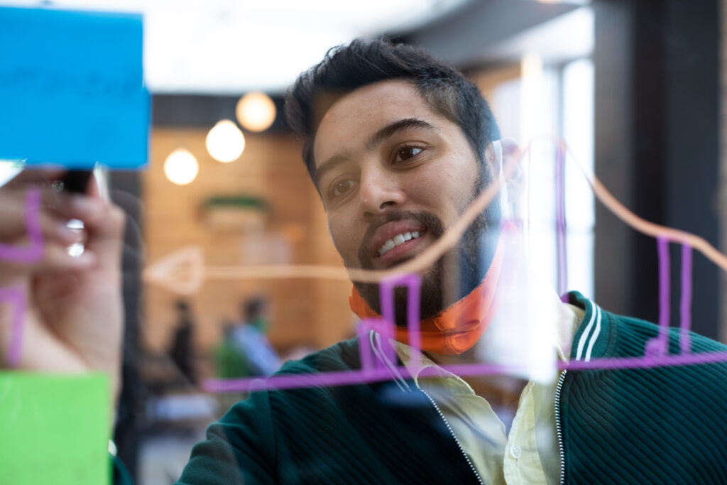 A young professional with a focused expression draws a colourful line graph on a transparent board. The graph, which appears to be a visual representation of data trends, is part of a discussion on how to check organic traffic.